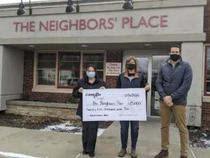 Three people standing outdoors, presenting a check for $25,000 to The Neighbor's Place staff. 