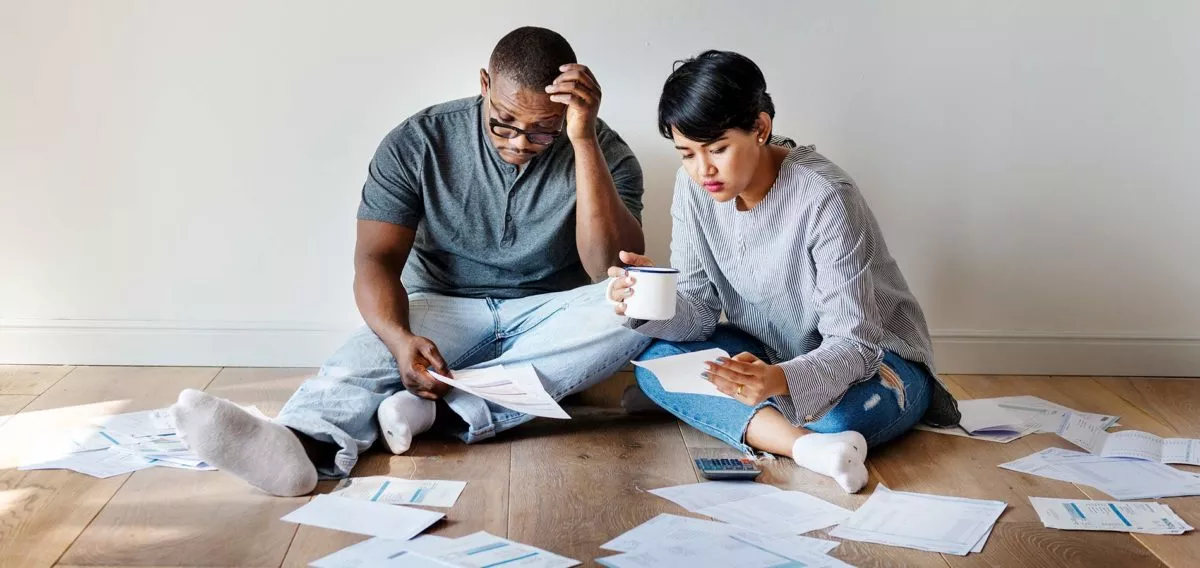 Two people sitting on the floor reading through financial statements.
